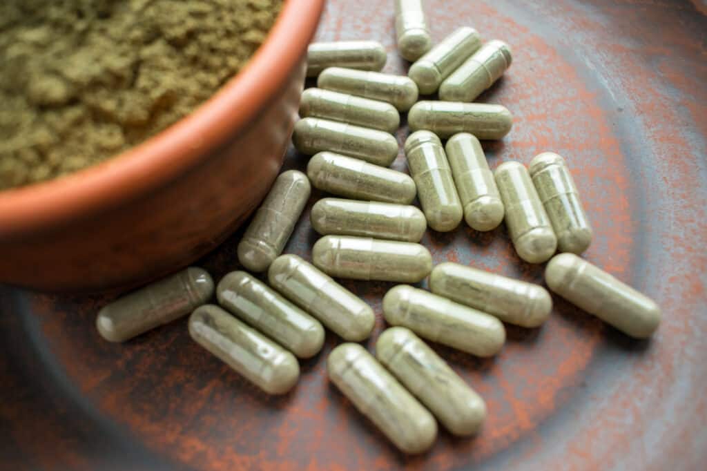 Supplement kratom green capsules and powder on brown plate. Herbal product alt-medicine kratom powder and kratom capsules. Close up. Selective focus