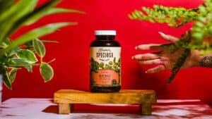 Super Speciosa Red Bali kratom capsules staged with red background and plants.
