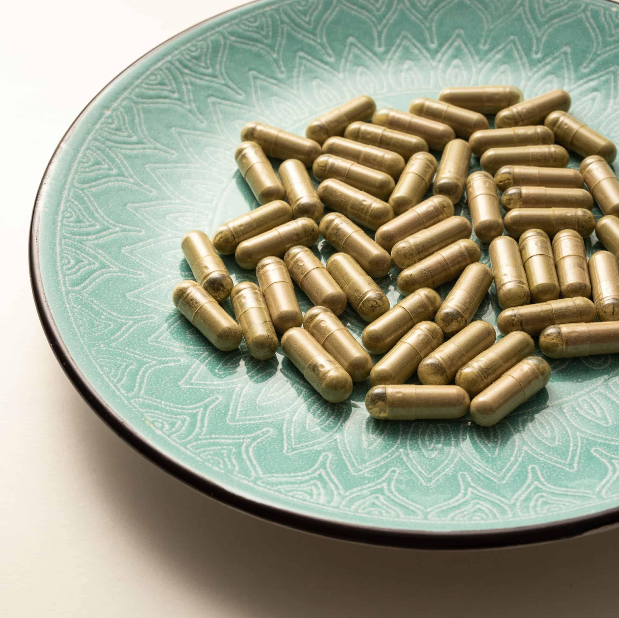 green plate with handful of kratom capsules laying randomly, selective focus