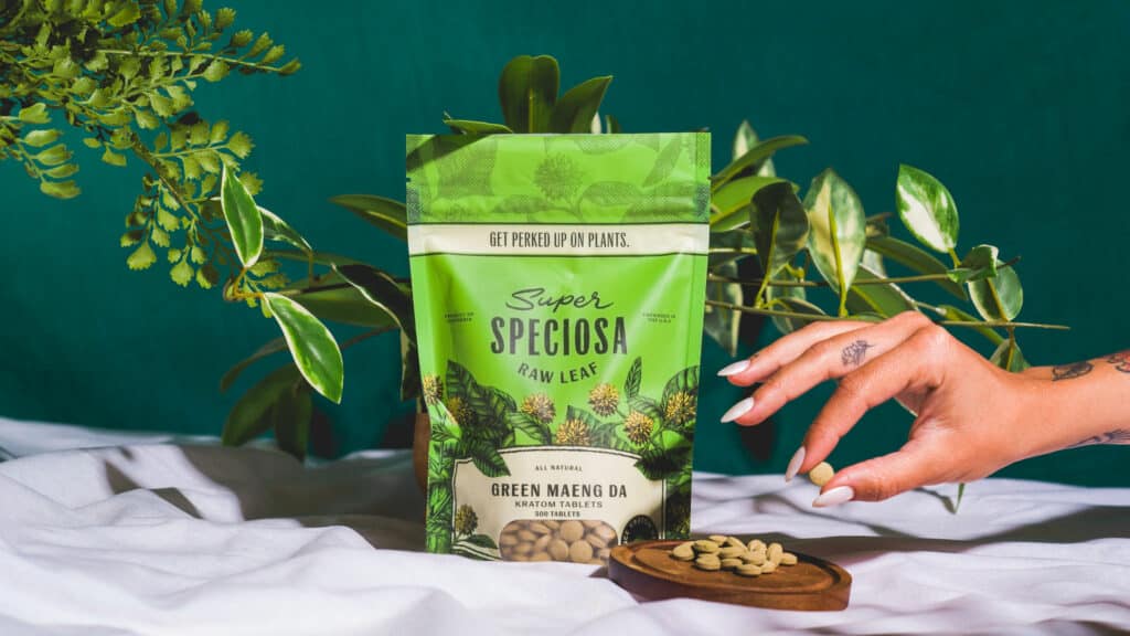 Super Speciosa's Green Maeng Da kratom tablets, stylized with greenery and woman's hand picking up kratom tablet.