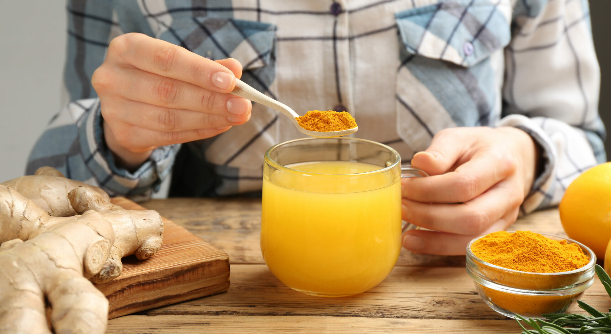 Woman adding turmeric to immunity boosting drink at wooden table with ingredients, closeup. Turmeric is a powerful kratom potentiator.