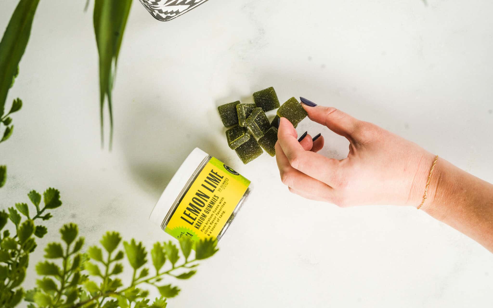 Hand reaching out to Super Speciosa Lemon Lime Kratom Gummies made with premium kratom extract.