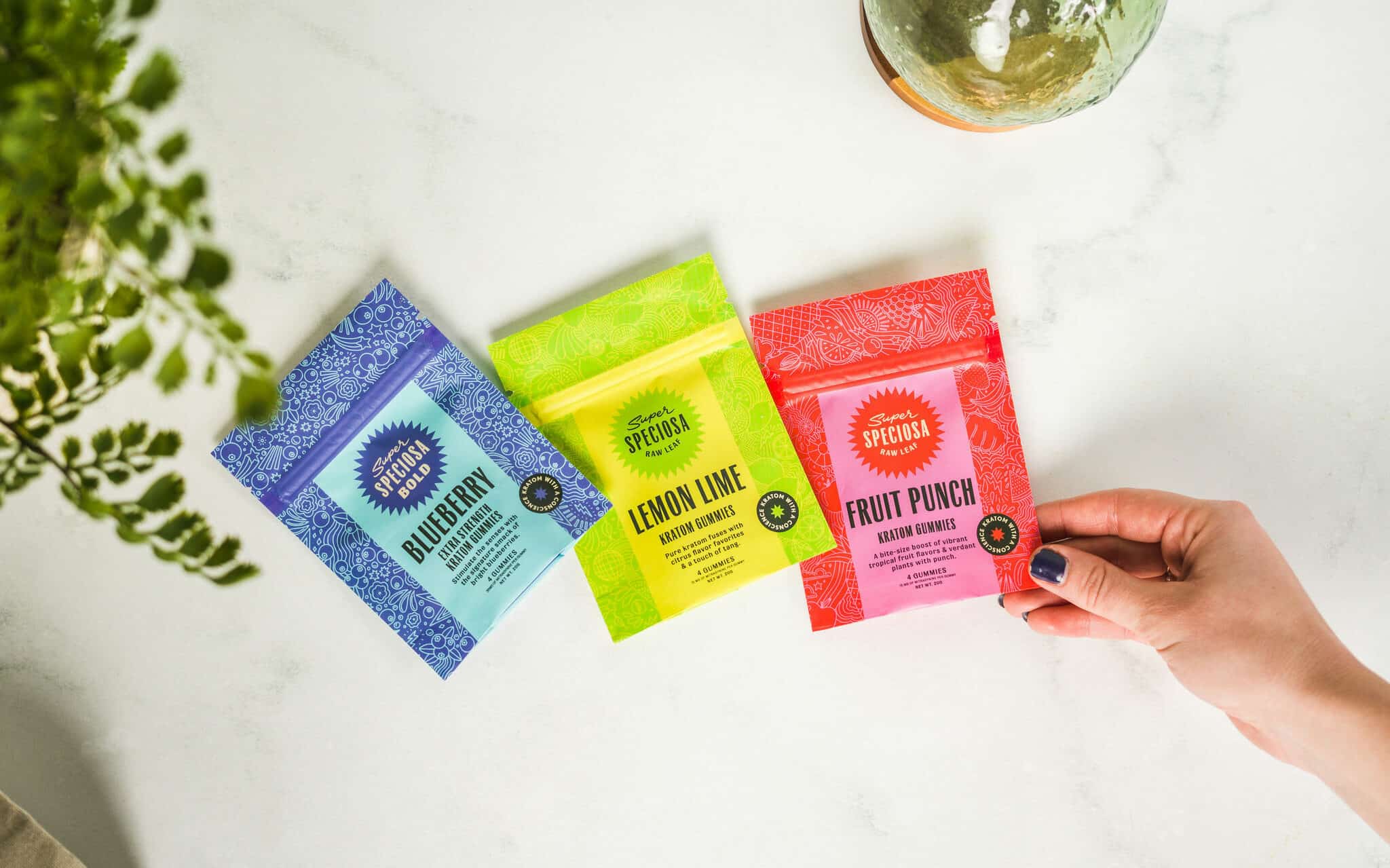 Selection of Super Speciosa Kratom Gummies and hand reaching out to gram them. Read this blog on how to choose the right kratom gummies for you!